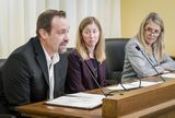 Matt Stupnik sits at the testifiers' table and speaks into a microphone to someone out of view. Jamie Fitzke and Representative Christensen sit next to him and watch as he speaks.